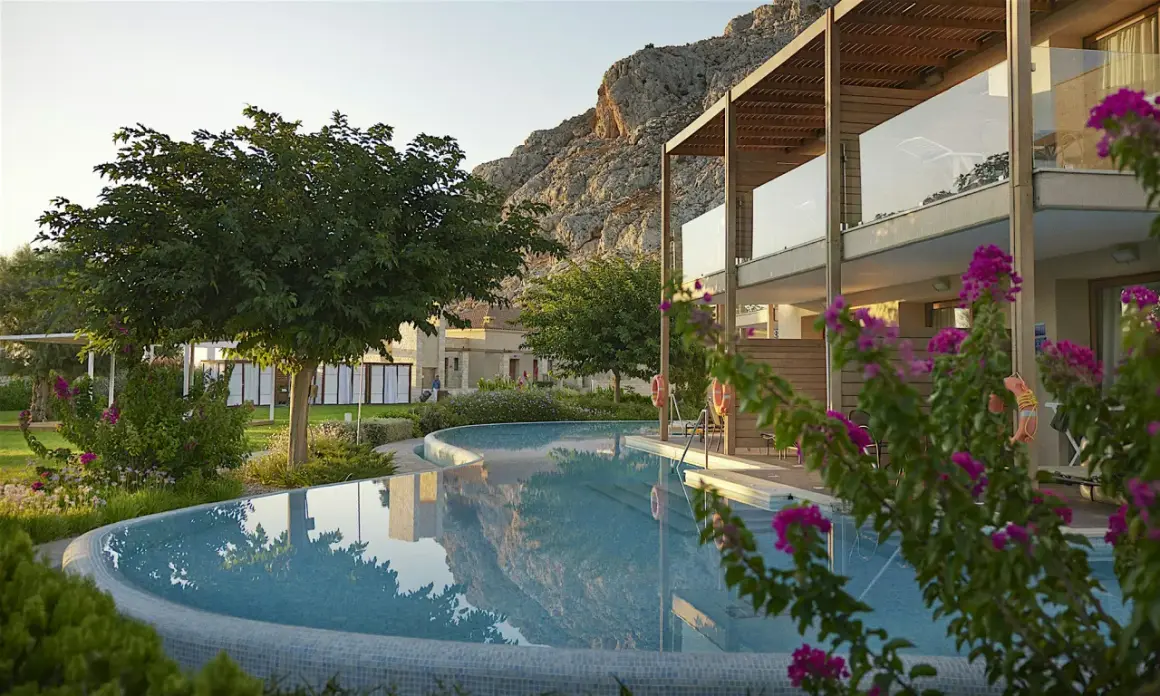 En vacker pool reflekterar bergen vid aegean park rhodos. Blommor och grönska omger hotellet.
