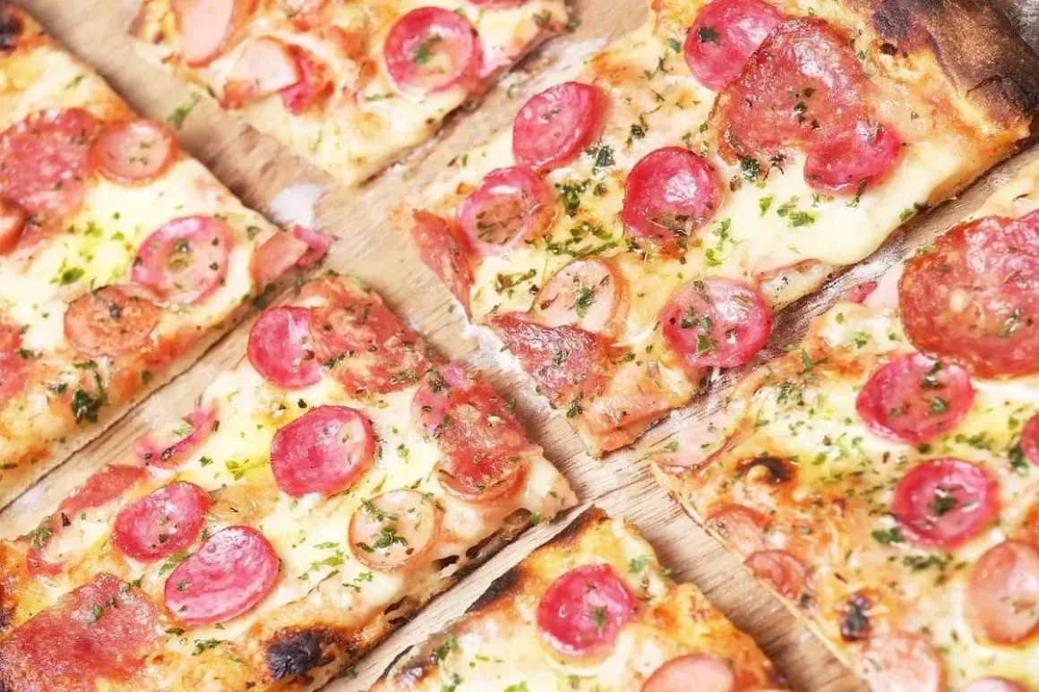 Kawałki pizzy z kiełbasą i serem, posypane ziołami. Idealne ciasto na pizzę dla każdego smakosza.