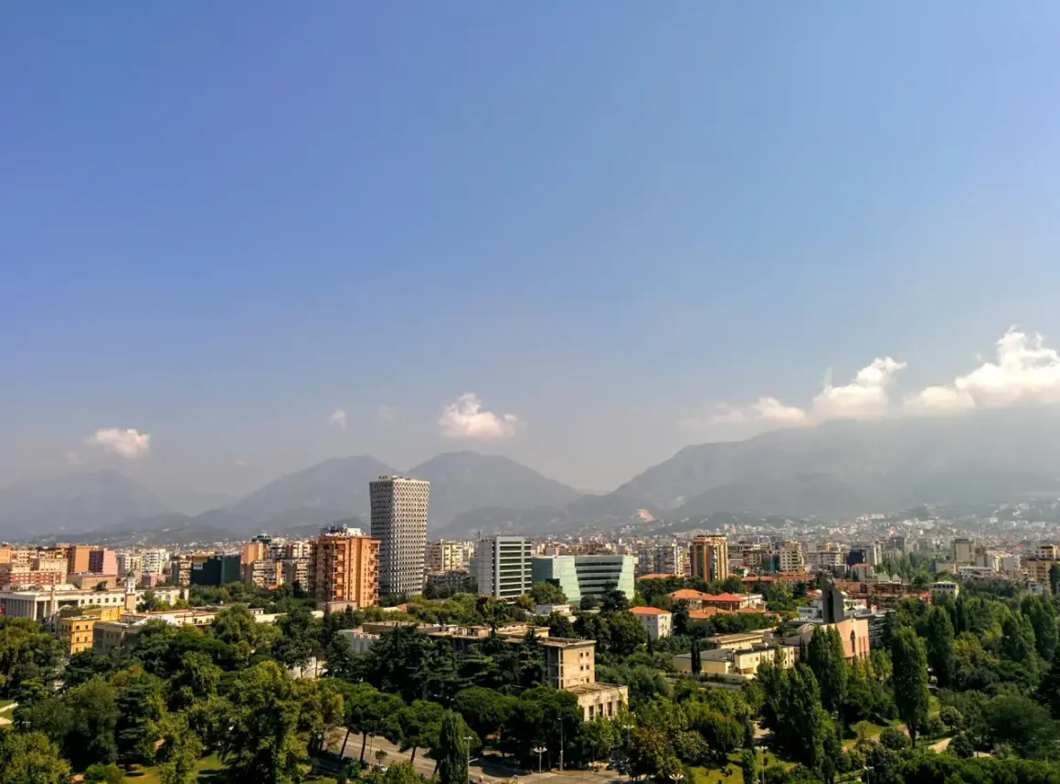 Widok na miasto z górami w tle. Widać nowoczesne budynki i zieleń. To ekuz Albania.