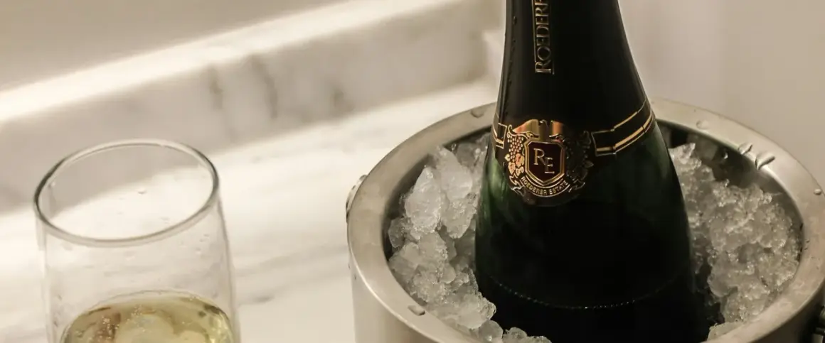Eine Flasche Champagner in einem Eisbehälter, daneben ein Glas mit prickelndem Wein. Perfekt gekühlt, wann gefriert wein?