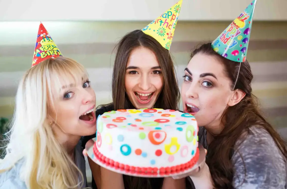 Tre amiche festeggiano con una torta colorata, pronte a soffiare le candeline per un addio al nubilato indimenticabile.