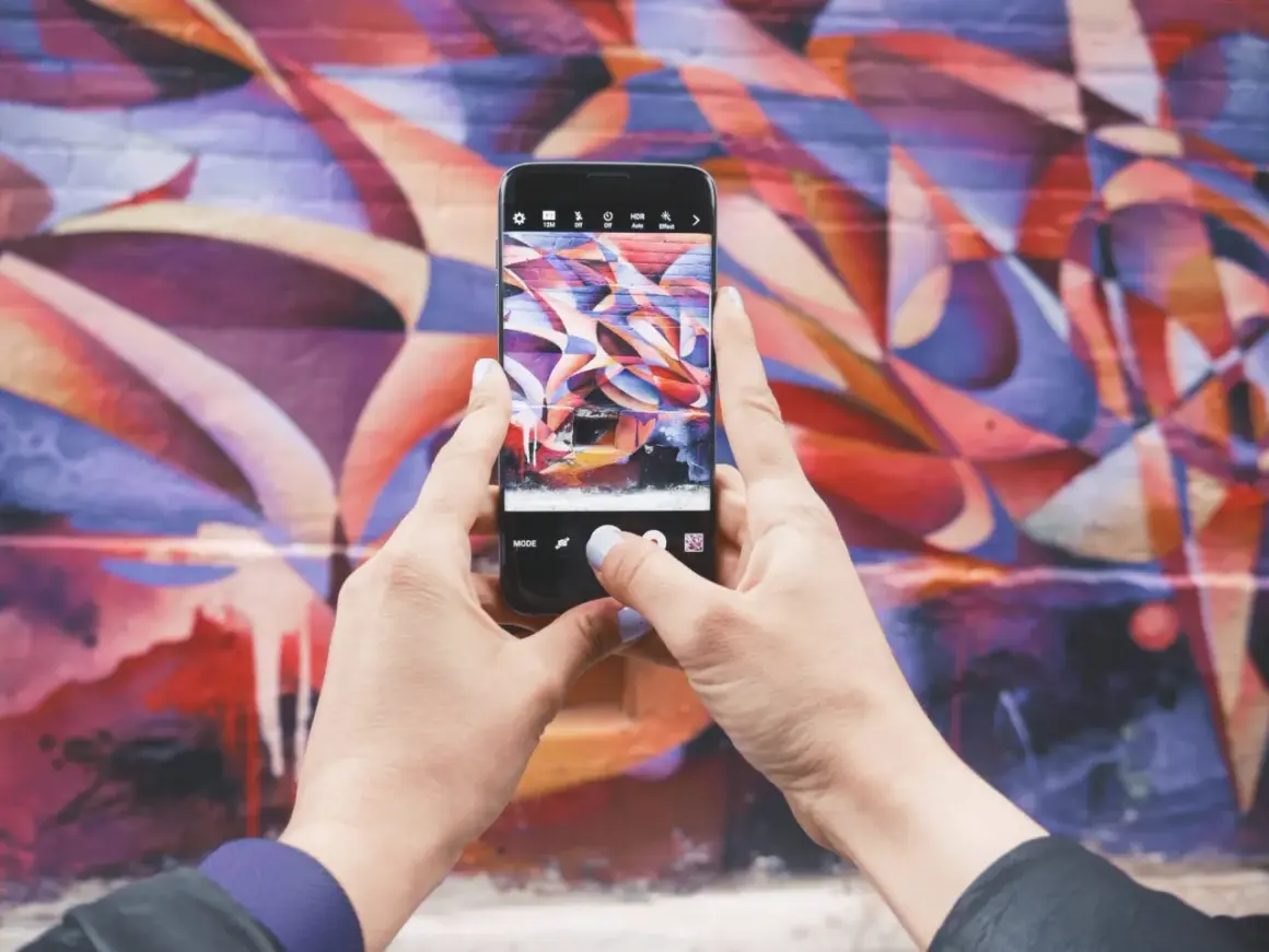 Zdjecie na Instagrama: ręce trzymają telefon, robiąc zdjęcie kolorowego muralu.