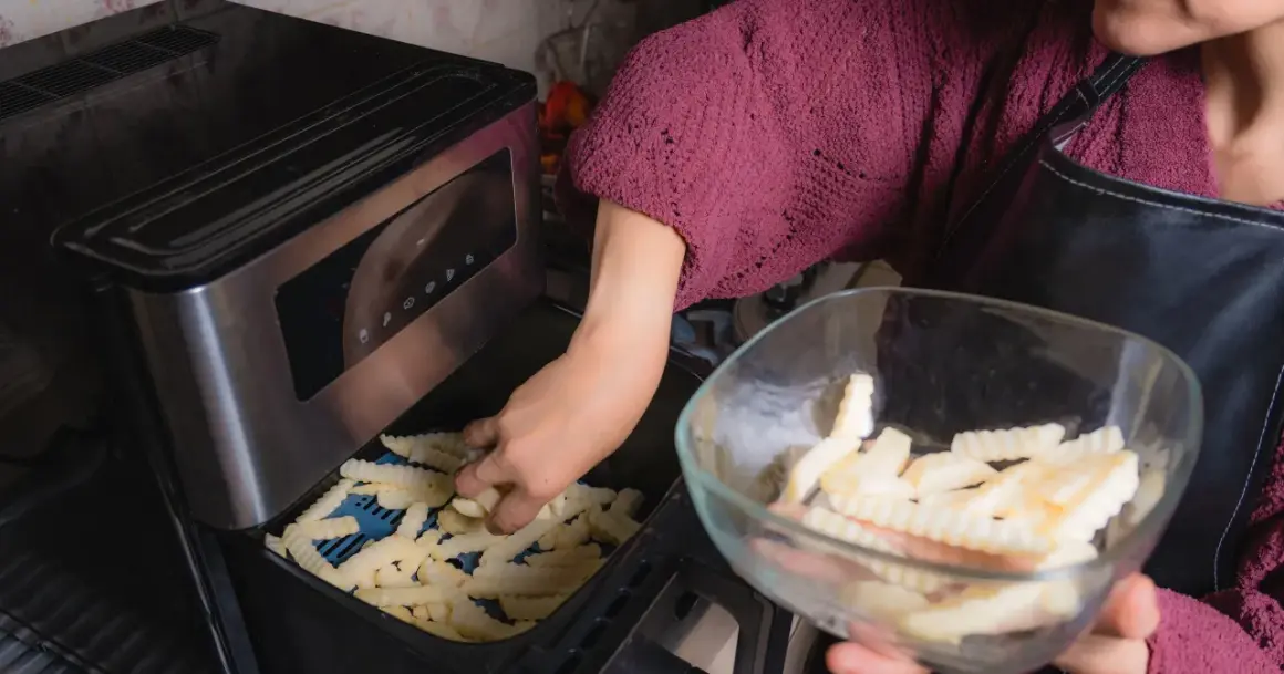 Ręka wkłada frytki do frytkownicy, przygotowując pyszne dania z airfryer przepisy po polsku.