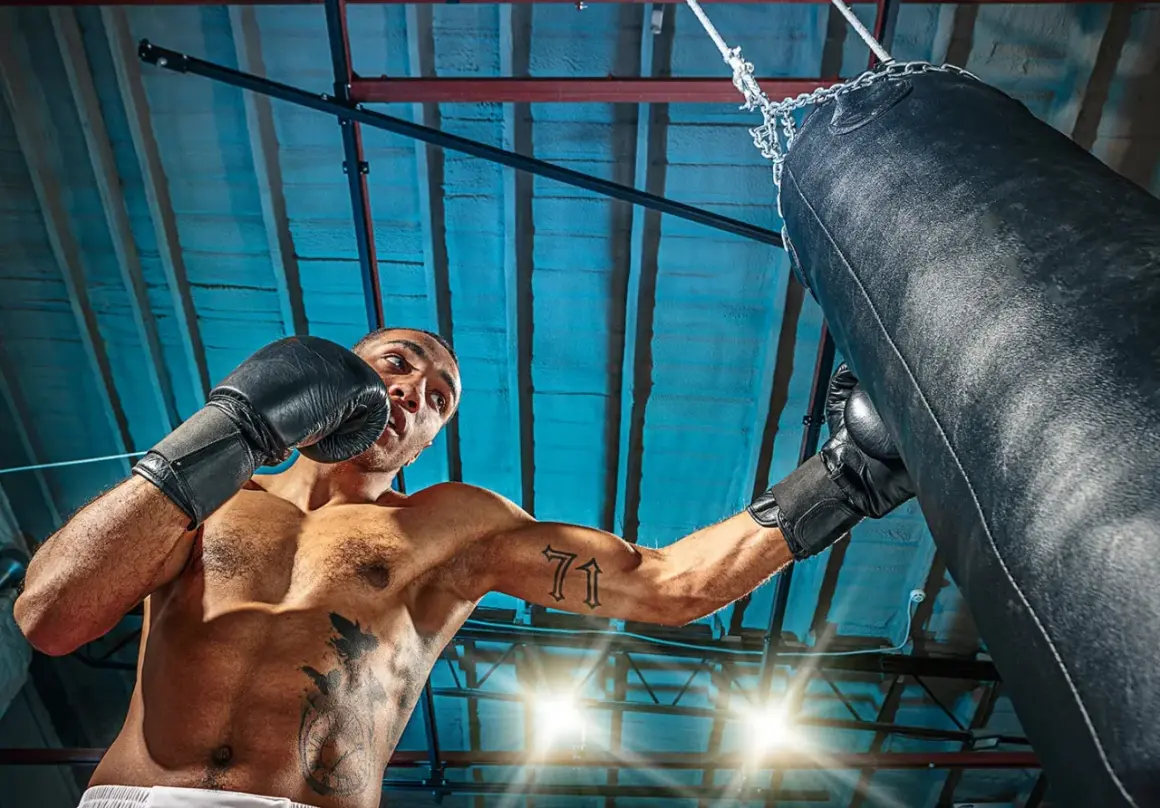 Man i boxningshandskar tränar sparra boxning mot en sandsäck i ett gym.