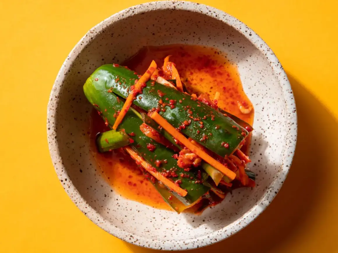 En skål med kimchi gurka, kryddad med chili och morot, på en gul bakgrund.