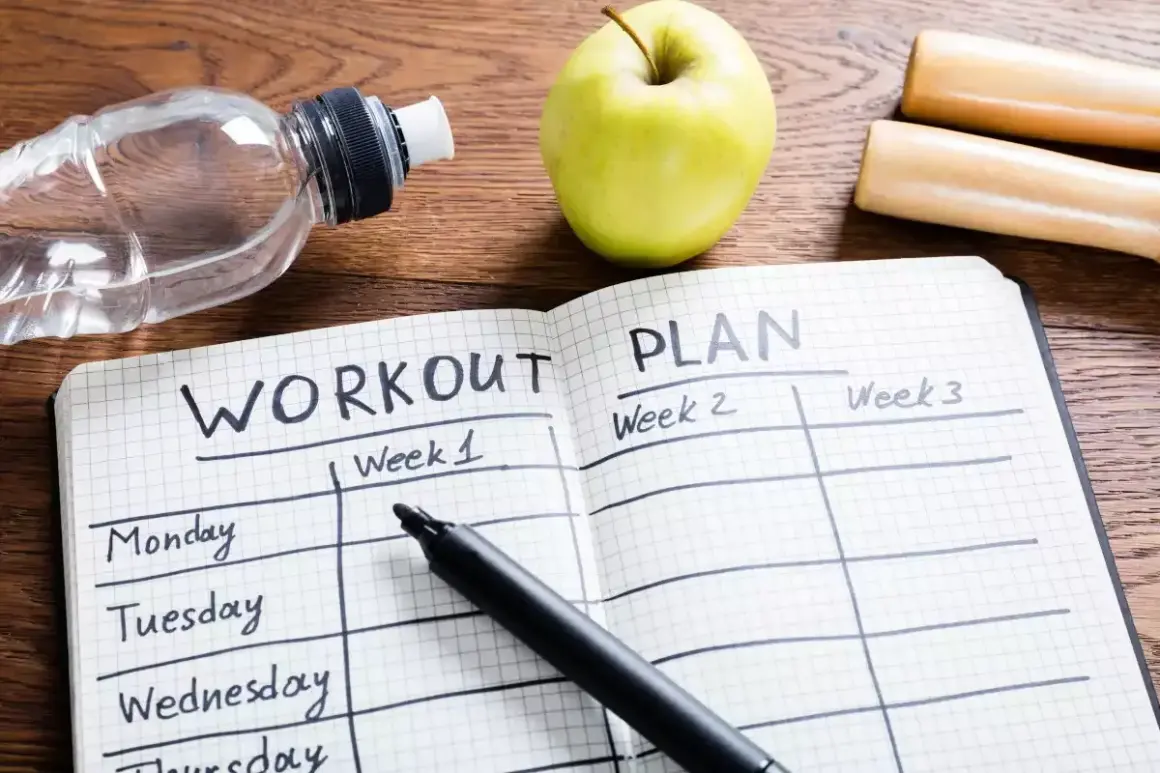 Plan na **full body workout** w zeszycie, obok jabłka, butelki wody i hantli.