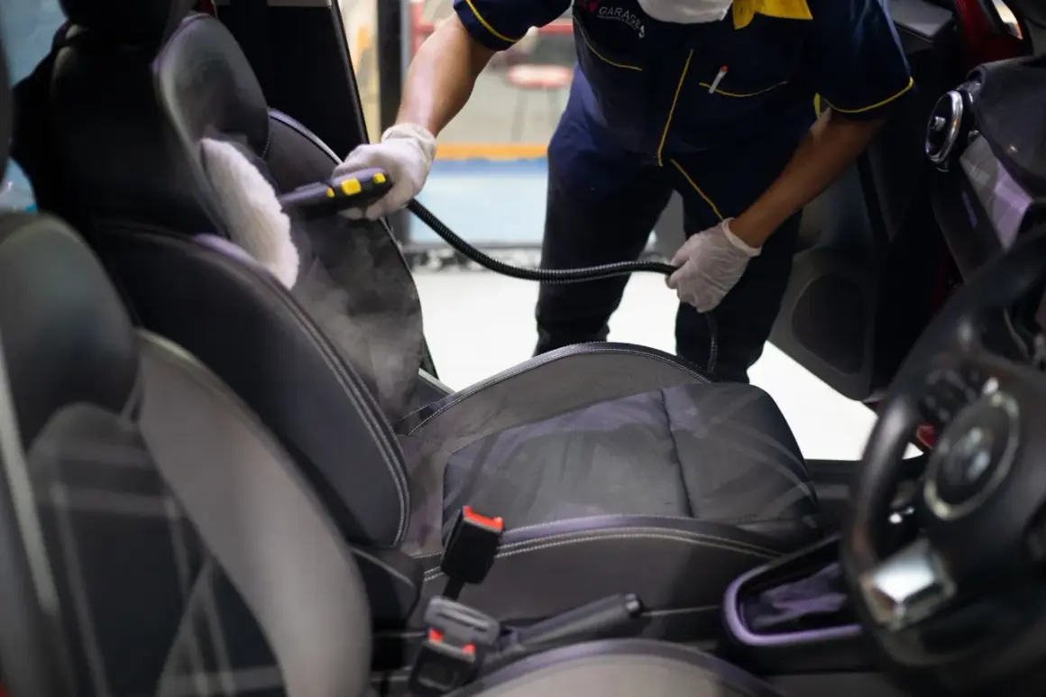 Profesional usando vapor para limpiar los asientos del coche. El vapor ayuda a eliminar manchas y desinfectar.