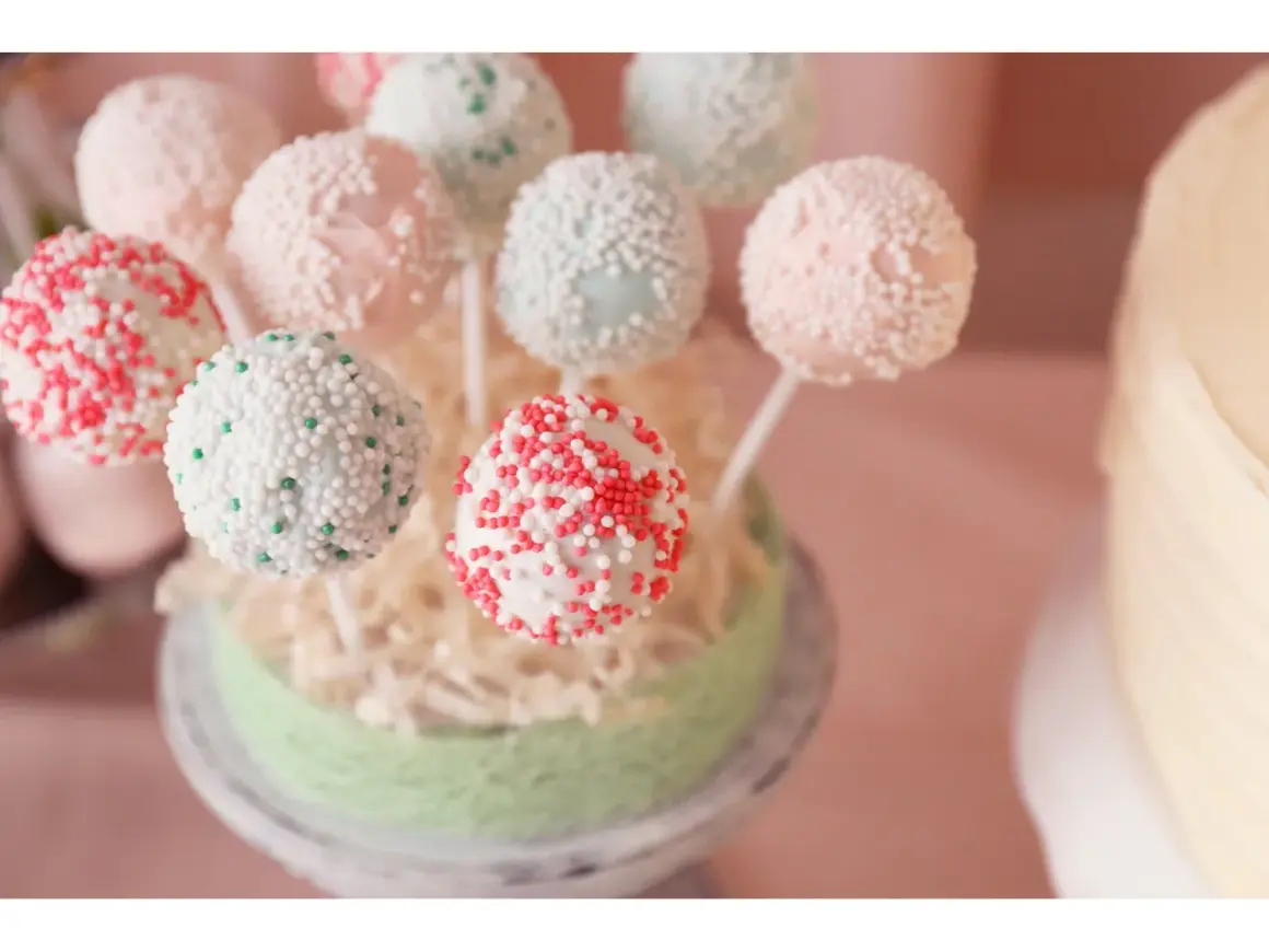 Bunte Kuchen am Stiel, verziert mit Perlen und Streuseln, auf einem grünen Podest arrangiert.