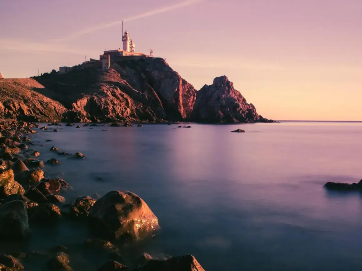 Faro en Cabo de Gata al atardecer, con rocas en primer plano y el mar en calma. Un lugar perfecto para disfrutar de la tranquilidad, como en el bar La Estrella.