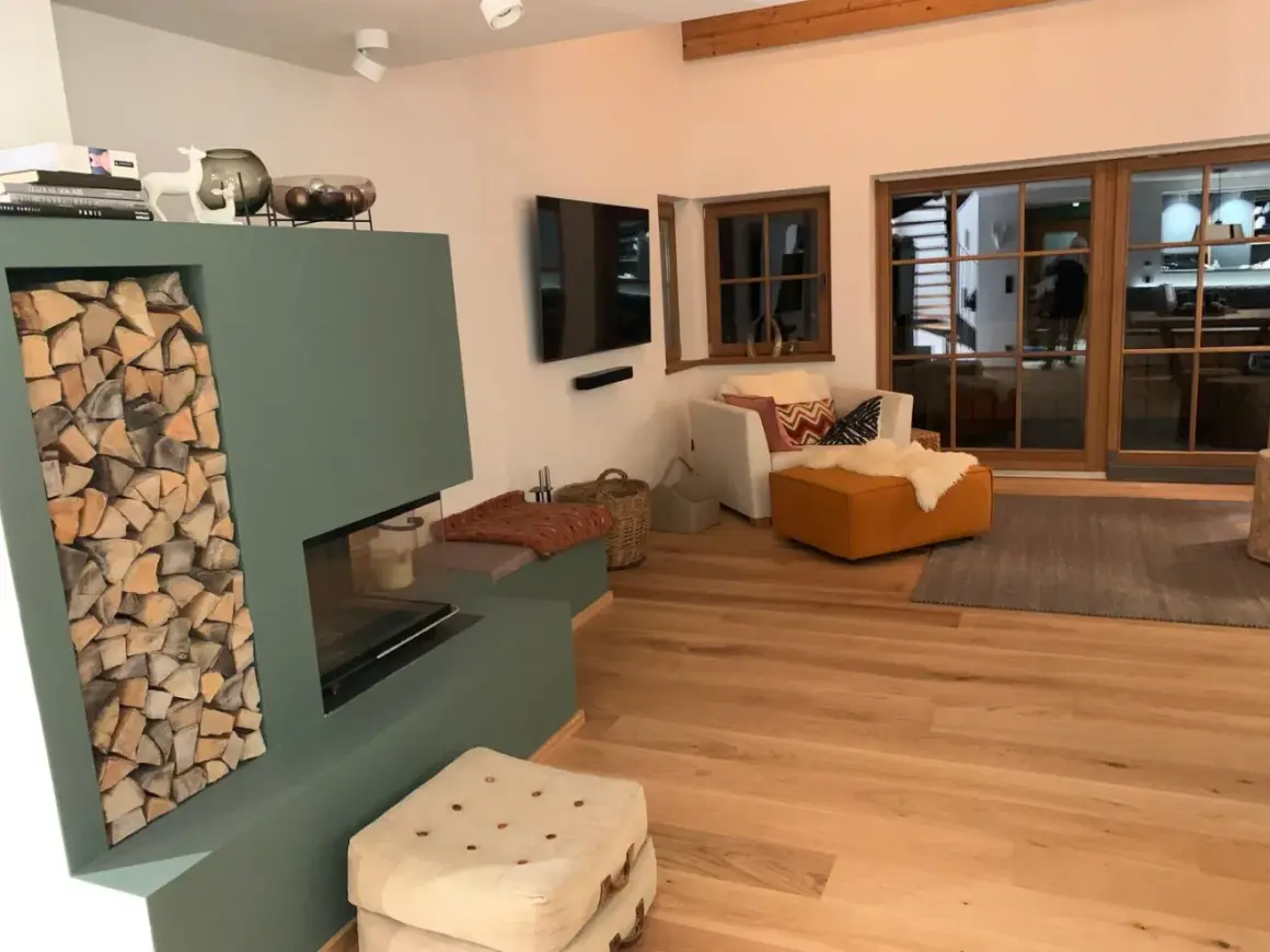 Gemütliches Wohnzimmer im modernen Landhausstil mit Kamin, Holzfußboden und großen Glasfronten.