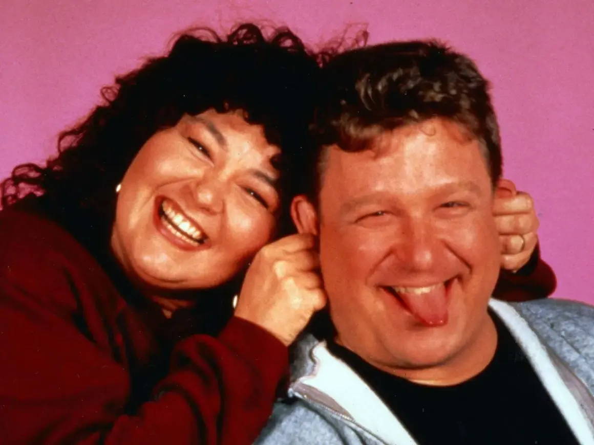 Roseanne und Dan, die Hauptfiguren der besetzung von Roseanne, lachen und Grimassen vor einem rosa Hintergrund.