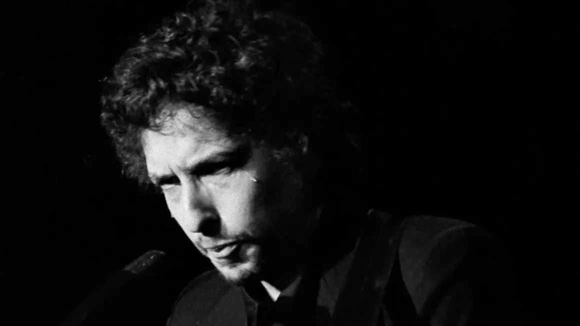 Bob Dylan, ikoniskt ansikte i en svartvit film, med lockigt hår och intensiv blick.