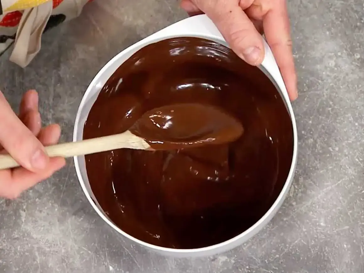 En sked rör i en skål med glansig choklad. Perfekt för ett enkelt ganache recept.