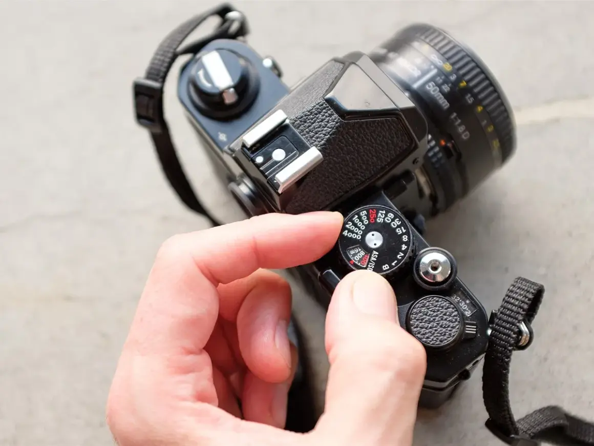 A hand adjusts the ISO dial on a vintage film camera, showing its mechanical controls.