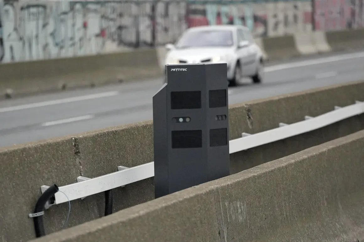 Un nouveau radar noir surveille la route. Une voiture passe en arrière-plan.