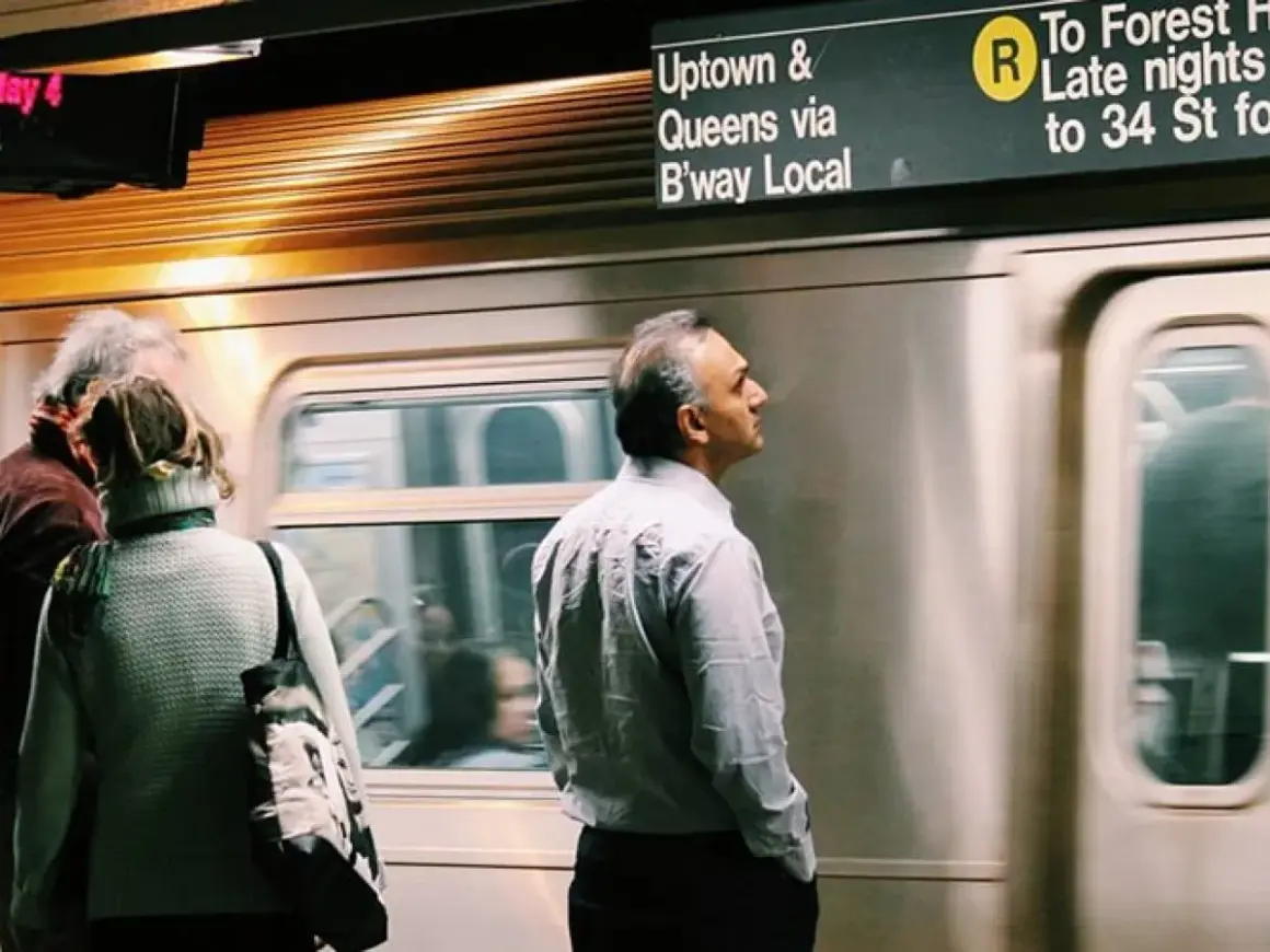 Personas esperando un tren en el metro de Nueva York con un letrero de destino.