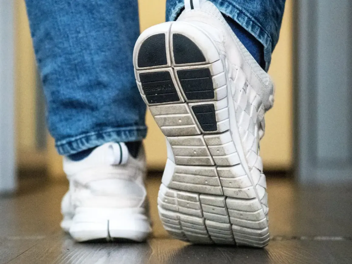 Nahaufnahme von weißen Turnschuhen mit Jeans. Die Sohle eines Schuhs ist deutlich zu sehen, bereit für den nächsten Schritt, der vielleicht quietschende Schuhe hinterlässt.
