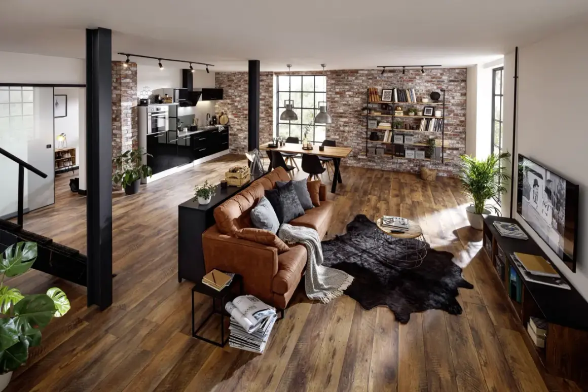 Geräumiges Wohnzimmer im industrial style mit brauner Ledercouch, Holztisch und Ziegelwand.