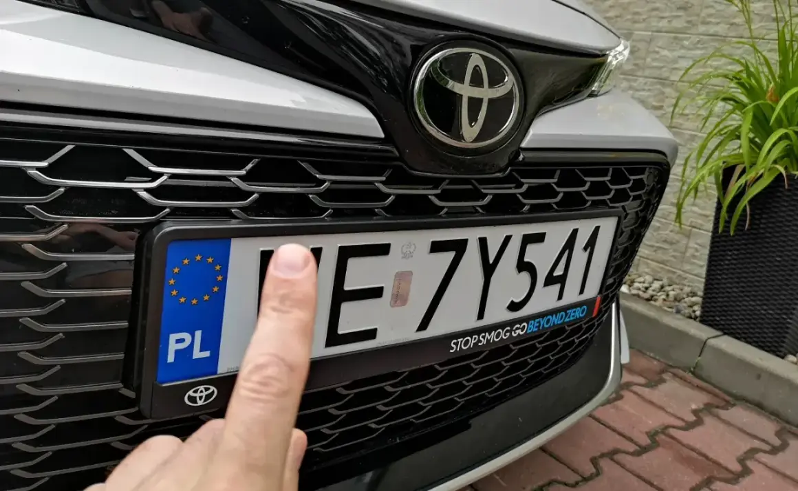 Palec wskazuje na tablicę rejestracyjną samochodu, która wygląda na zgubioną.