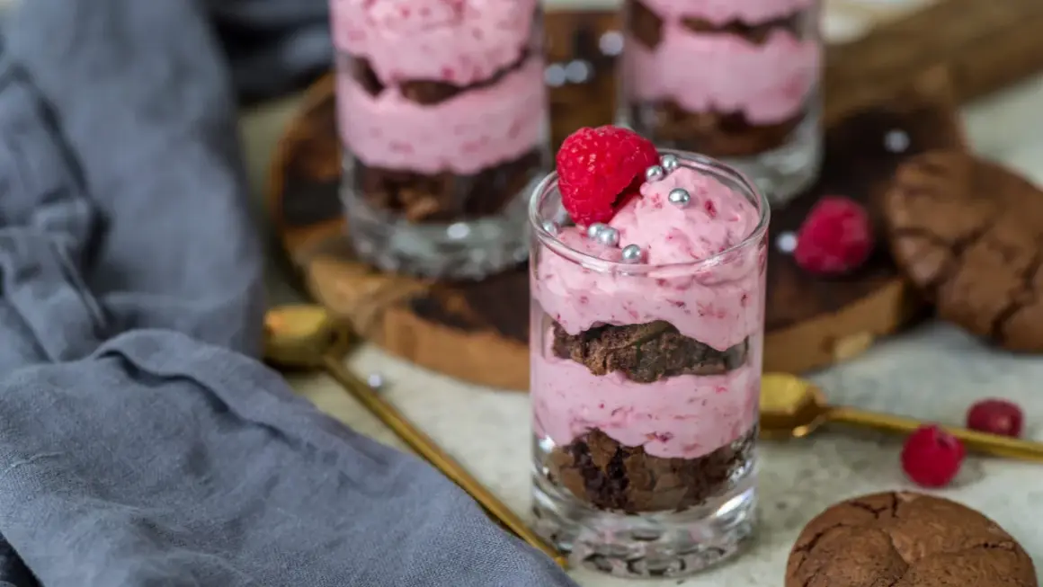 Ljuvlig hallonmousse till tårta i glas, varvad med chokladkaka och toppad med färsk hallon och silverkulor.