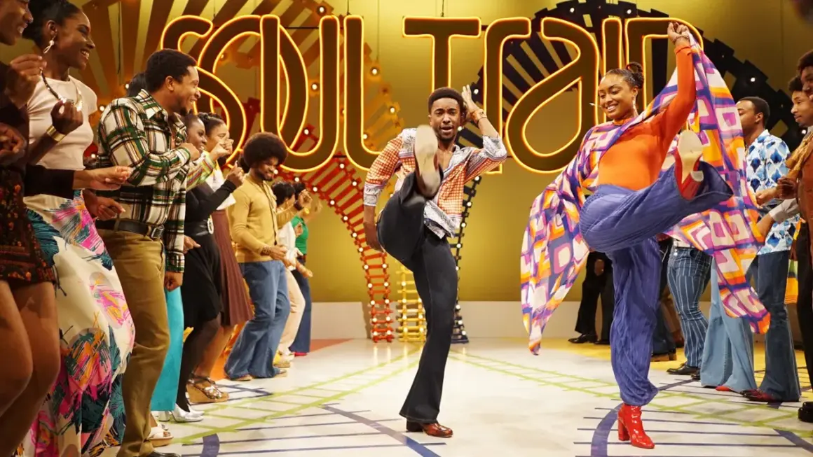 Ballerini in abiti colorati danzano sul palco di Soul Train, con un uomo che fa un calcio in aria e una donna che volteggia con uno scialle.