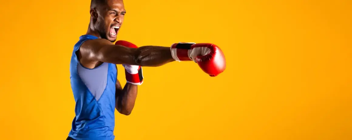 A boxer in a blue tank top throws a punch, his face contorted in a roar. He's ready to compete in the junior welterweight weight class.