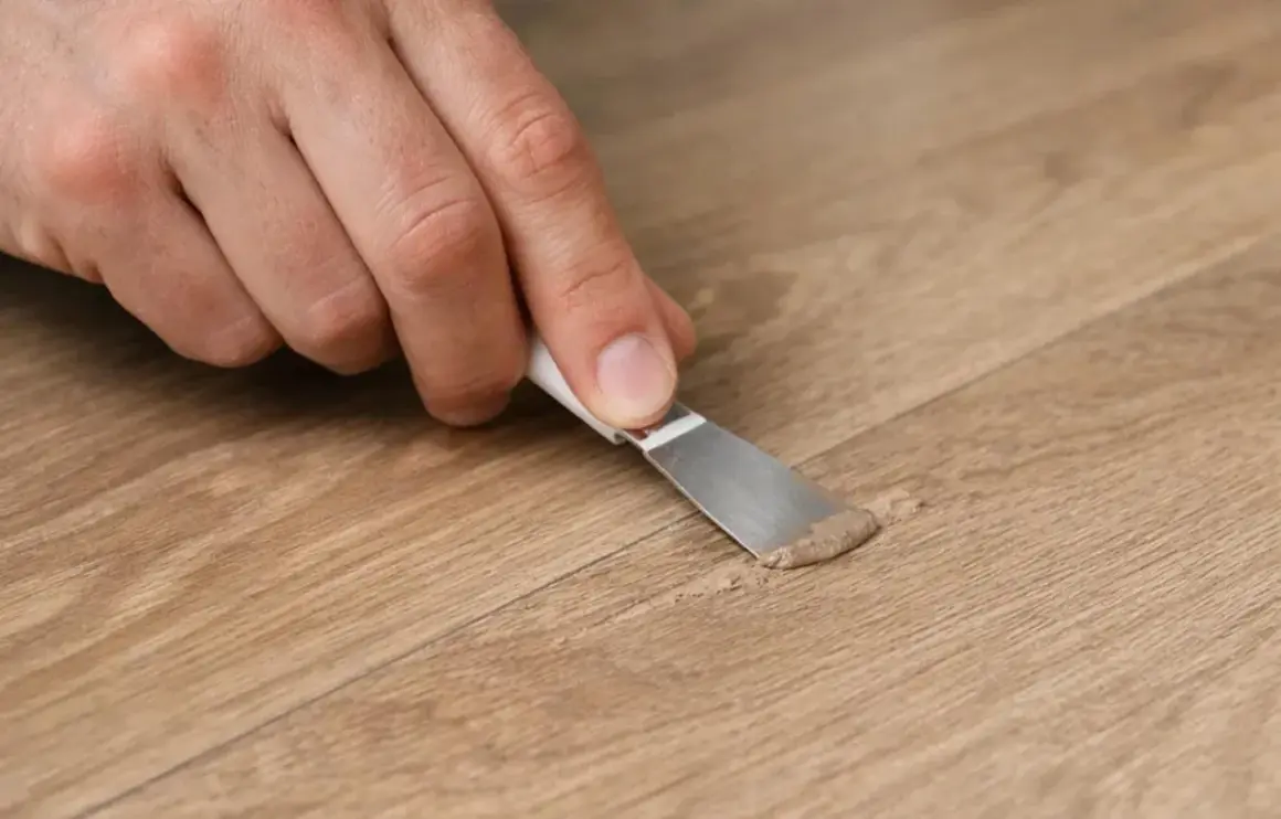 Mano che applica stucco per la riparazione parquet su una fessura del legno.