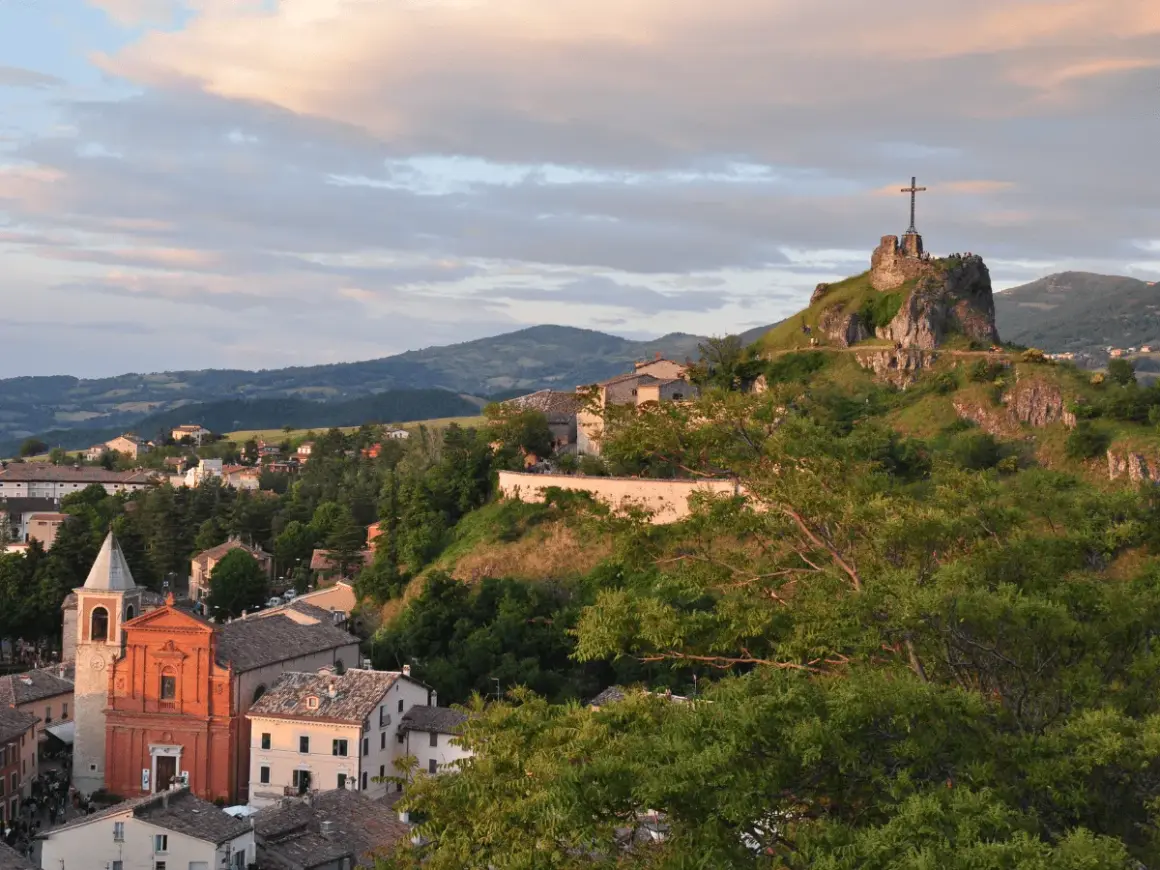 Panoramica di Pennabilli, Rimini, con la chiesa e la rocca con la croce che domina il paesaggio collinare al tramonto.