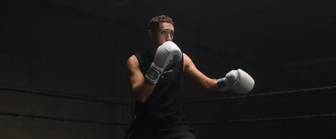 Boxer in white gloves practices a boxing slip in a dark ring, ready for the next round.