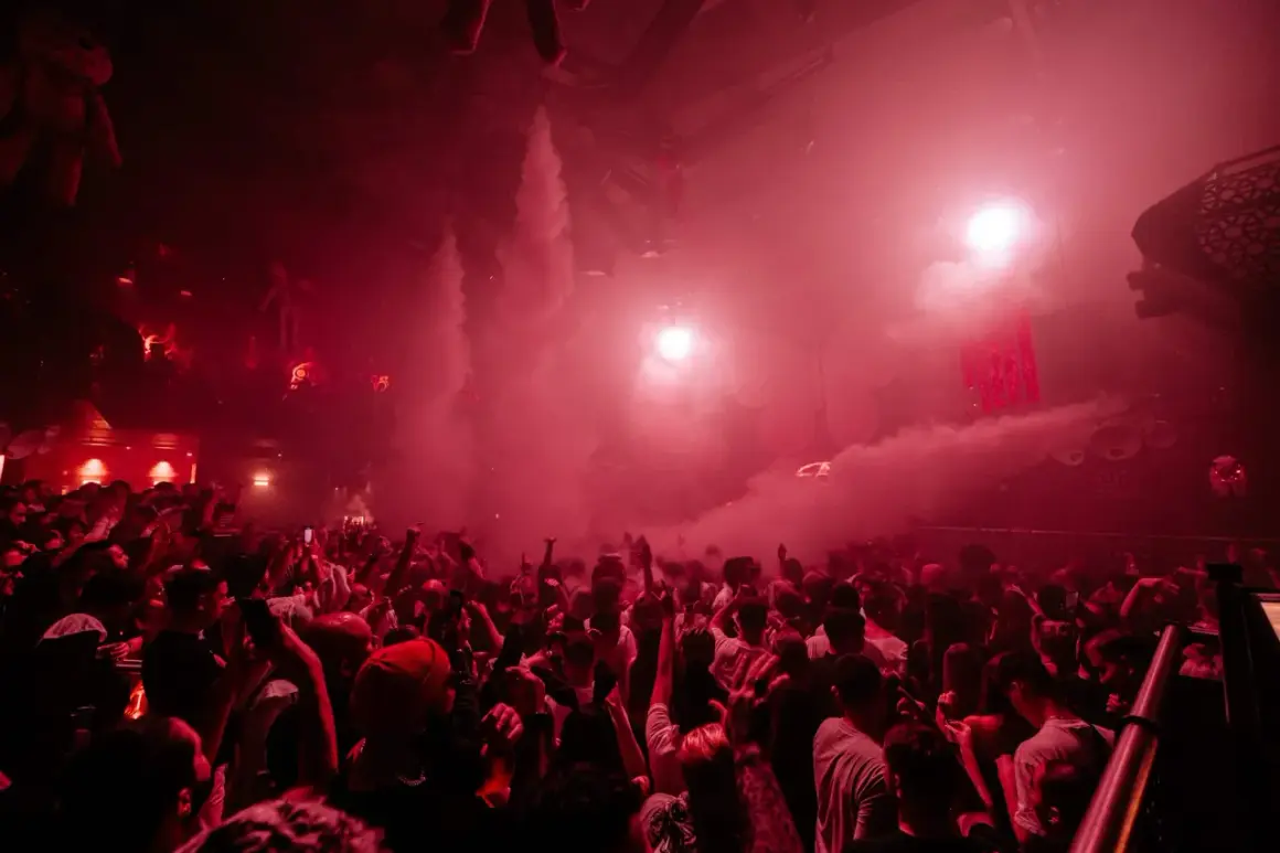 Folla in delirio in una discoteca di Londra, tra fumo rosso e luci stroboscopiche.