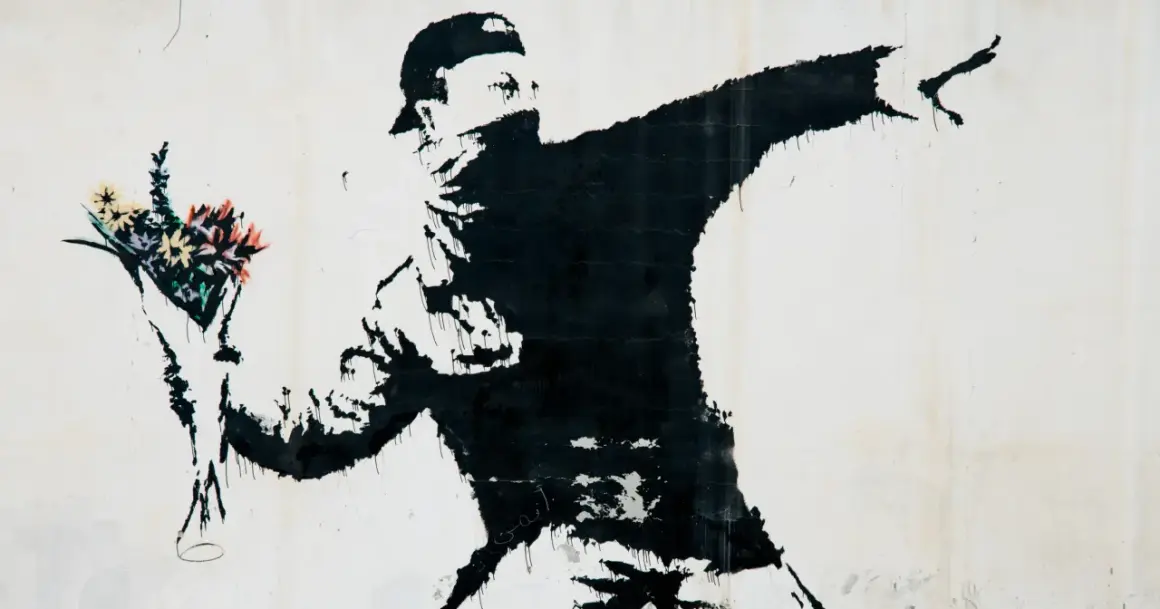 Czarny mural przedstawia zamaskowanego mężczyznę w czapce, rzucającego bukiet kolorowych kwiatów. To najładniejszy rysunek na świecie, pełen nadziei i buntu.