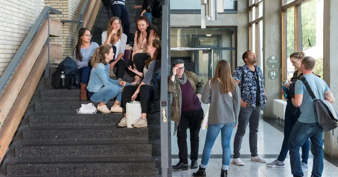 Studenten auf Treppen und im Flur. Eine Gruppe junger Leute, die sich auf einer Treppe unterhalten, vielleicht nach einem Kurs im berufsbegleitenden Studium Berlin.