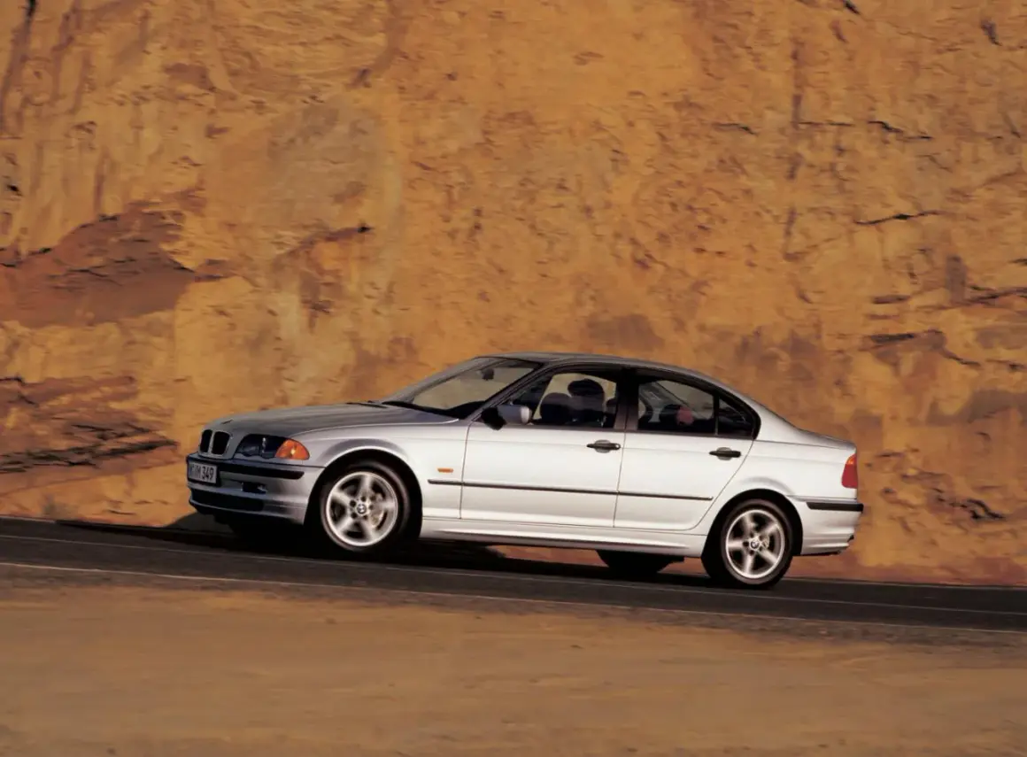 Srebrne bmw e46 330i sunie po drodze na tle skalistego, pomarańczowego zbocza.