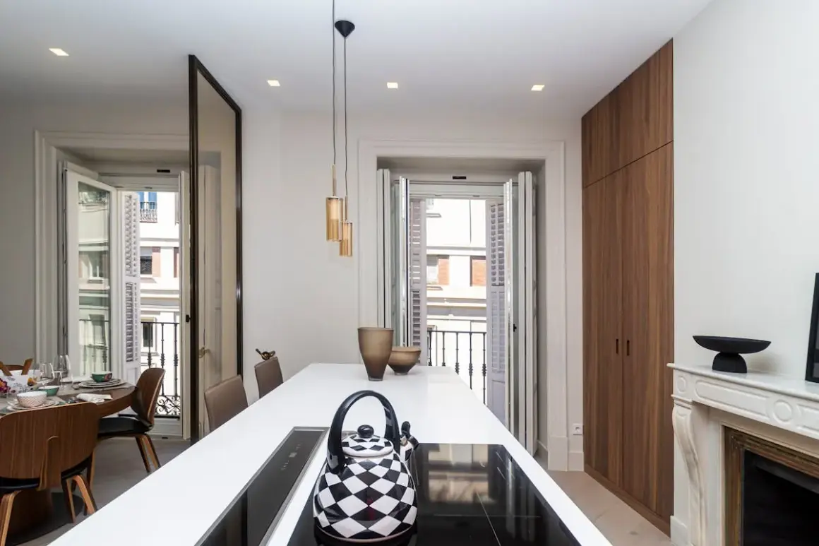 Cocina moderna con isla blanca, tetera a cuadros y vistas a balcón. Un buen lugar para vivir, pero ¿cuánto cuesta un alquiler en Madrid?
