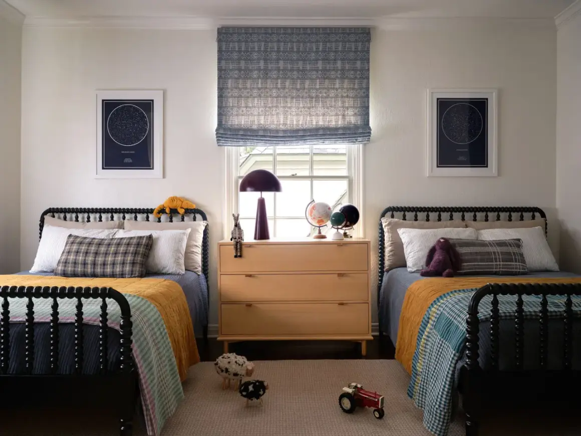 Twin beds with colorful quilts and star charts create fun boys bedroom ideas. A wooden dresser holds globes and a lamp.