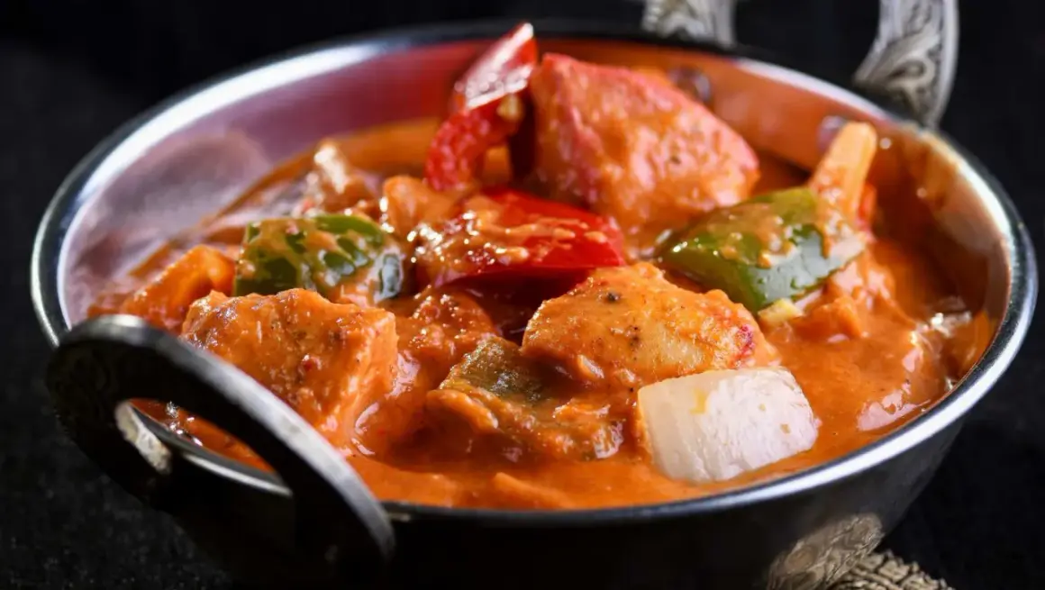 Delicioso pollo al curry con leche de coco, pimientos y cebolla en un cuenco metálico.
