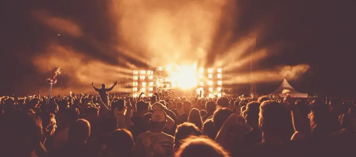 Tłum ludzi na festiwalu muzycznym, scena z jasnymi światłami i dymem.