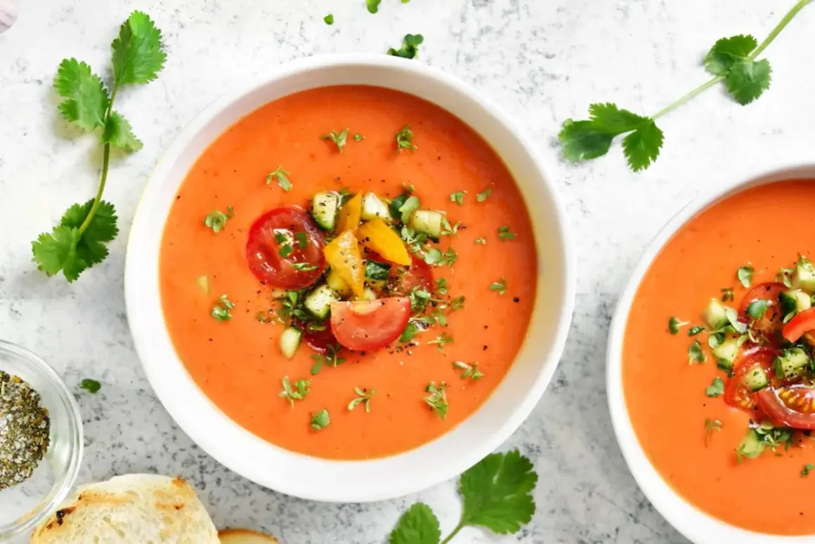Två skålar med krämig gazpacho, toppad med färska tomater, gurka och örter. Perfekt för ett lätt sommarmål.
