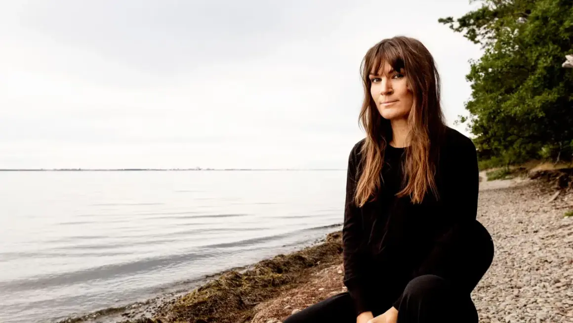 Malin Wollin sitter vid en stenig strand med havet i bakgrunden.