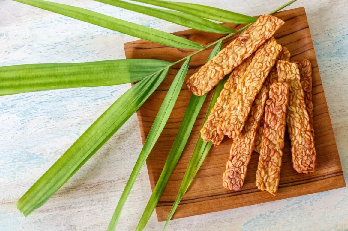 Knusprige Tempeh-Sticks auf einem Holzbrett, garniert mit grünen Blättern. Ein leckeres Tempeh-Rezept für gesunde Ernährung.