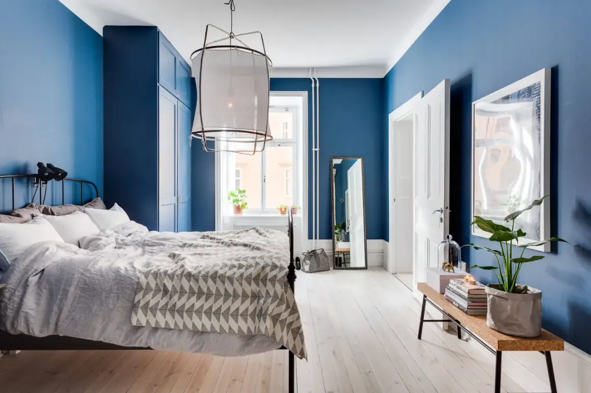 Camera da letto con accogliente parete azzurra, letto comodo, armadio blu e pavimento in legno chiaro.