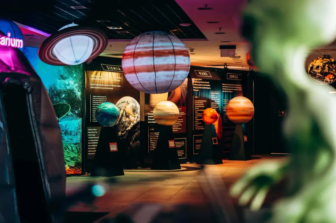 Modele planet i pierścieni Saturna w kosmo parku. W tle tablice informacyjne o Ziemi, Marsie i Jowiszu.
