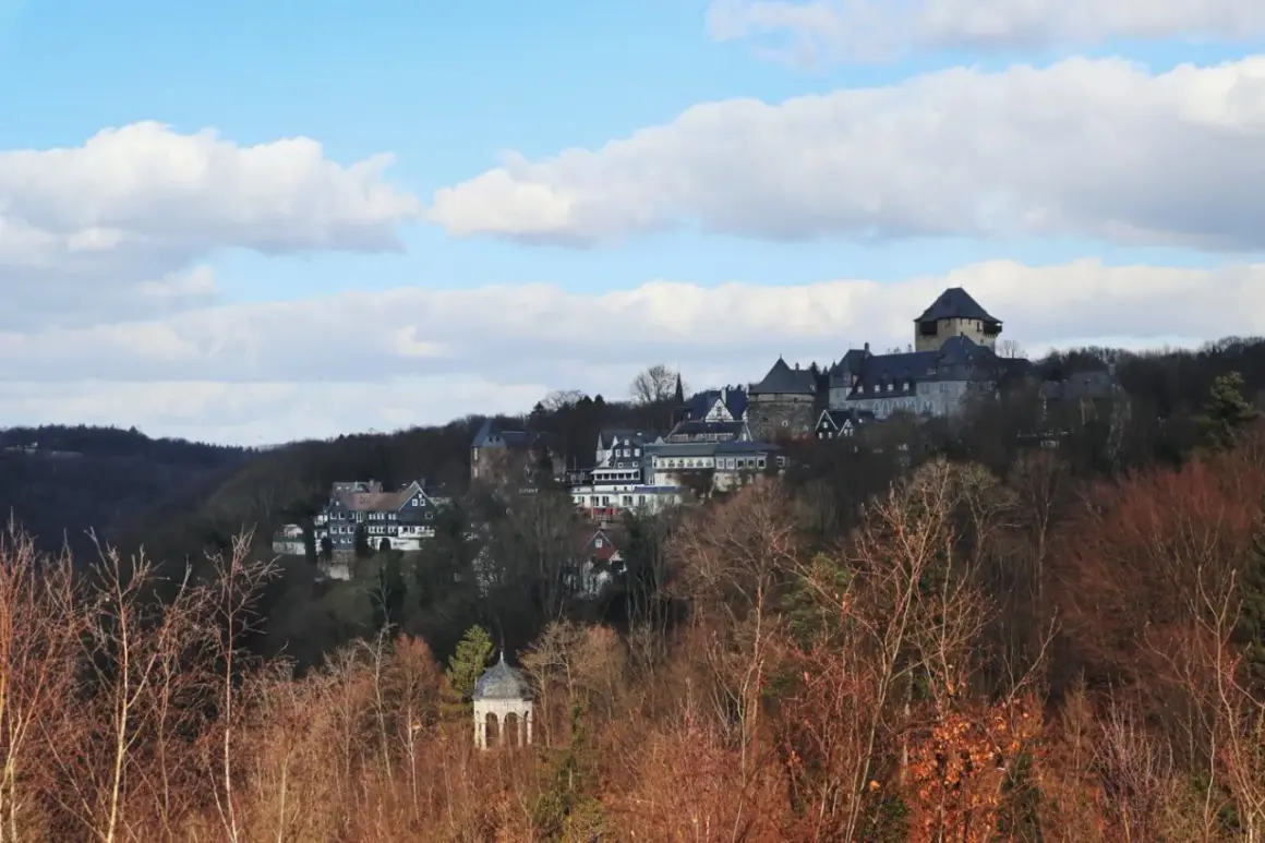 Blick auf Schloss Burg, das majestätisch auf einem Hügel thront, umgeben von Bäumen. Ein kleiner Pavillon im Vordergrund, im winterlichen Wupper Tal.
