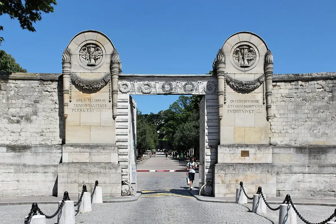 Monumentalna brama cmentarza Père Lachaise z łacińskimi inskrypcjami i płonącymi pochodniami.