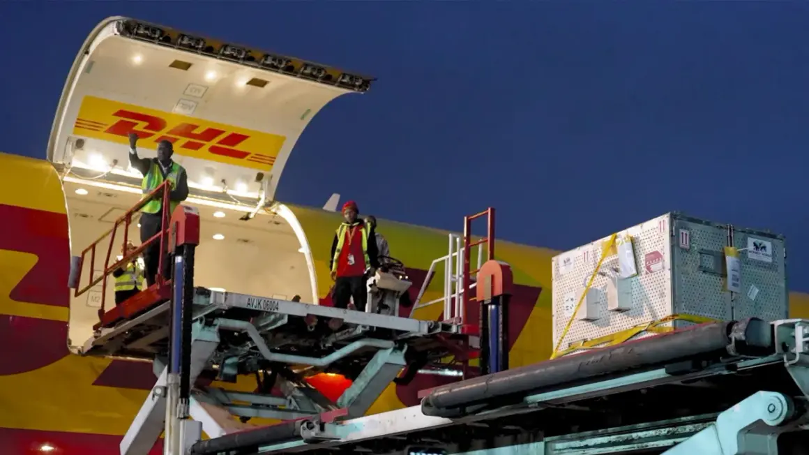 Pracownicy rozładowują samolot DHL. Z jakiego kraju pochodzi ten transport?