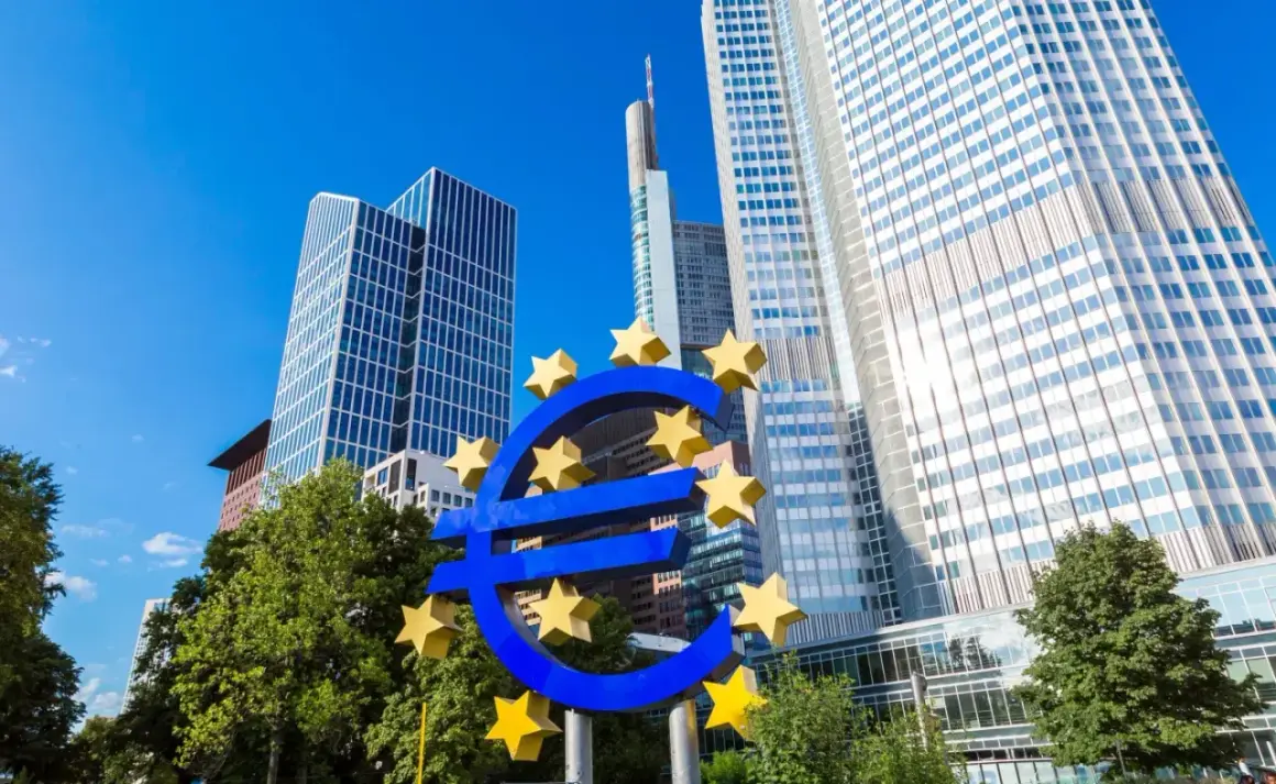 Symbol euro przed nowoczesnymi wieżowcami, siedzibą europejskiego banku centralnego.