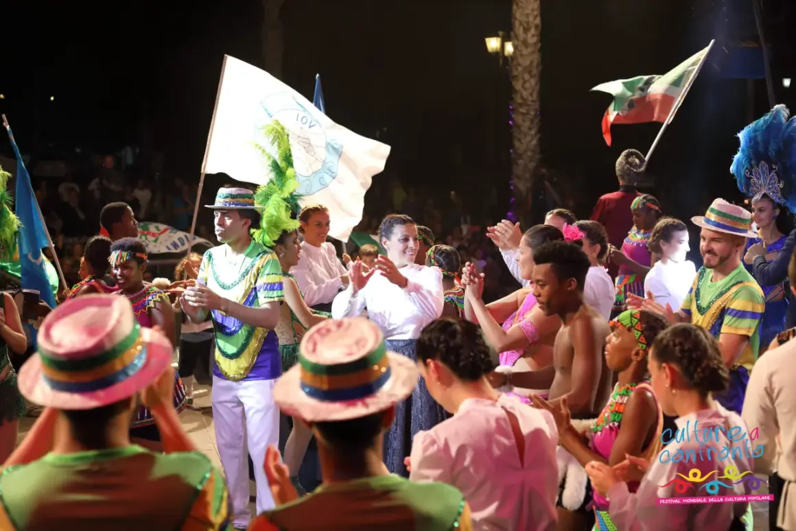 Gruppi calabresi famosi in festa, con costumi colorati e bandiere, celebrano la cultura popolare in un festival vivace.