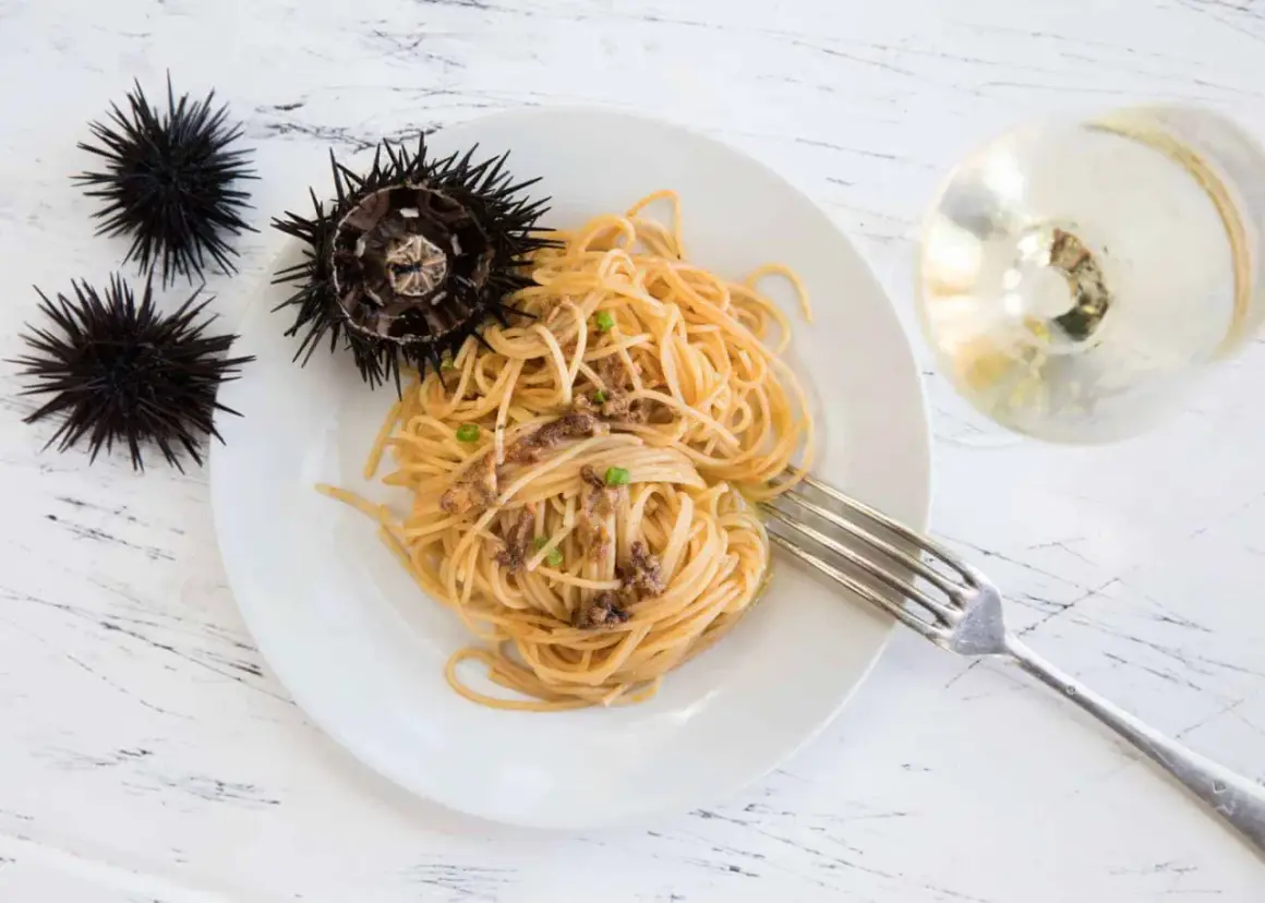 Seeigel-Spaghetti auf einem Teller, daneben rohe Seeigel. Man kann Seeigel essen und sie sind eine Delikatesse.