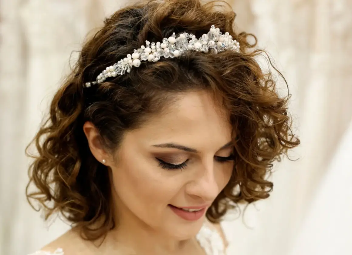 Brautfrisur kurze Haare Bob mit funkelndem Diadem. Lockige Haare umrahmen das Gesicht einer lächelnden Braut.