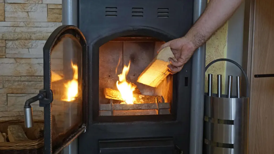 Hand legt Holzscheit mit gutem Brennwert Birke in den brennenden Ofen.